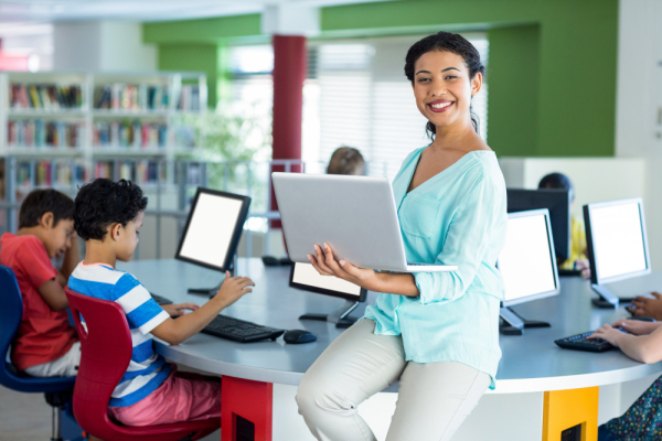 a happy teacher with students using laptop in the background